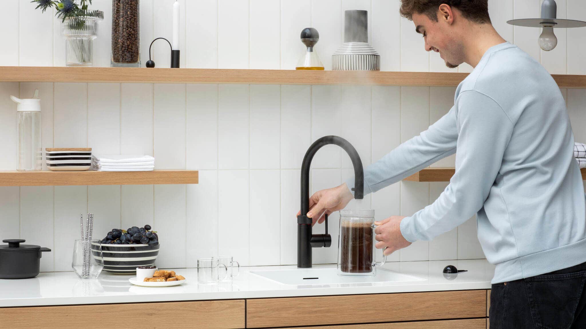 5 gode grunner til å velge en Quooker, en mann tapper kokende vann i kaffekannen fra sin Quooker Flex svart matt kran