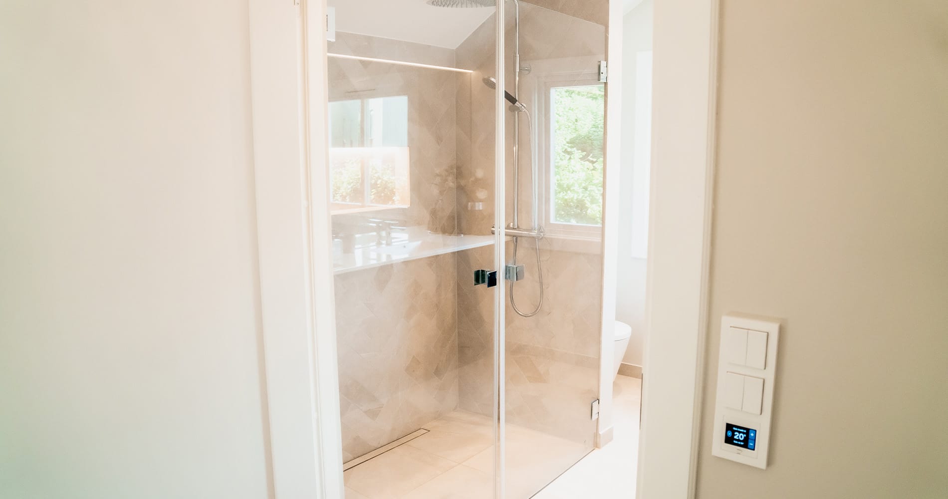 Romslig dusjsone med glassvegger og Vikingbad Rainshower i krom.Nyoppusset bad i varme, lyse toner med mørkt baderomsmøbel og blanke kromdetaljer.